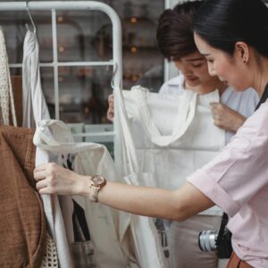 Two women examining eco-friendly bags in a fashionable boutique setting, highlighting sustainable shopping.